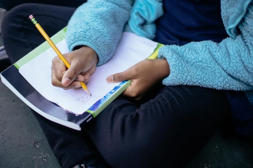 Student writing practice notes in a notebook with a pencil