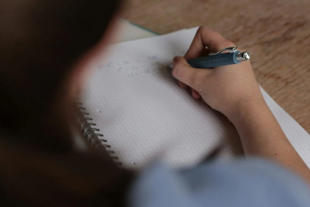 Student writing in a notebook with a pen