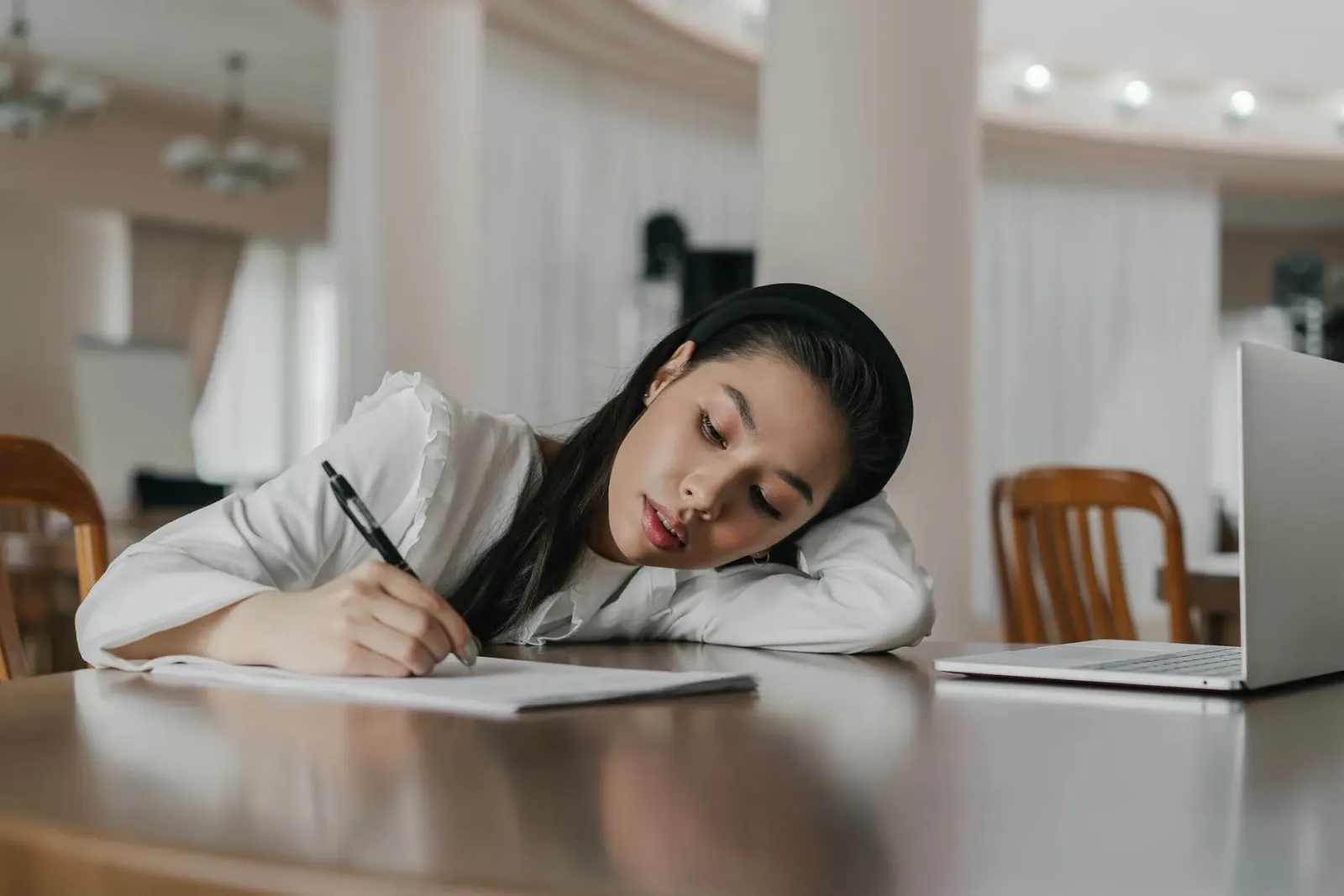 a woman in white long sleeves writing on paper