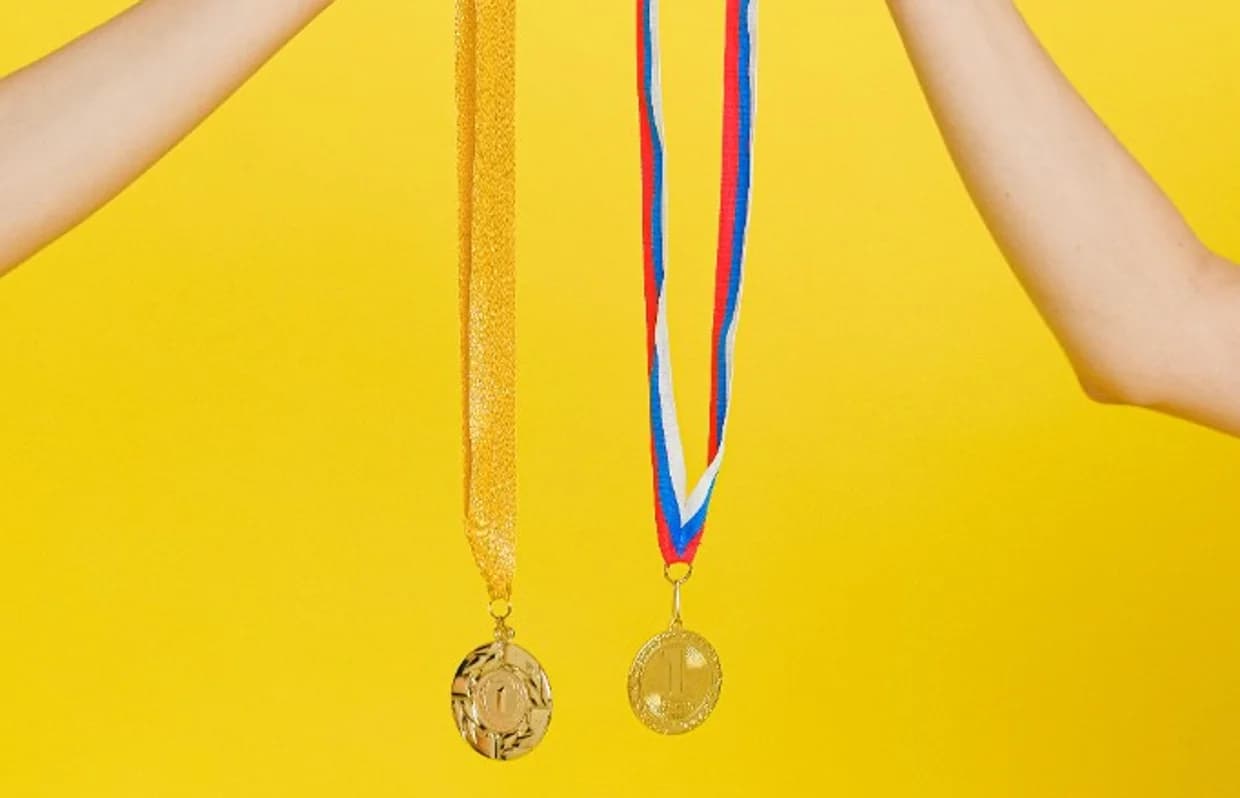Two gold first-place medals held up against a yellow background