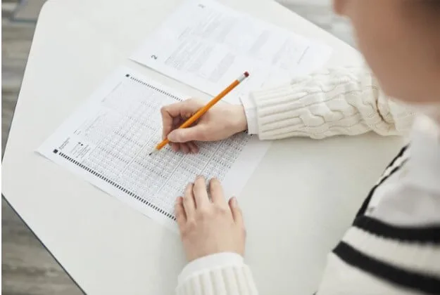 Photo shows a girl filling in an answer sheet with a pencil.