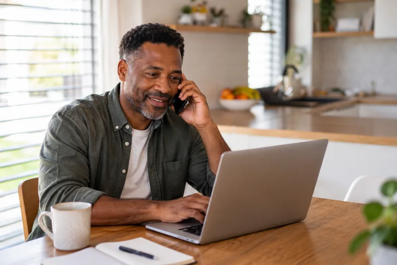 A parent on a call at a laptop in a home kitchen