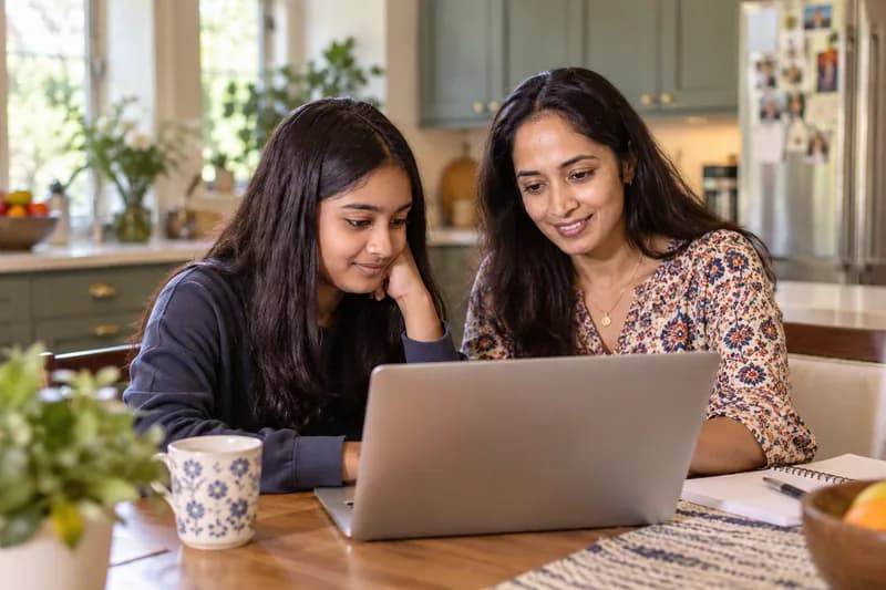 A parent and student looking at a laptop together at the kitchen table